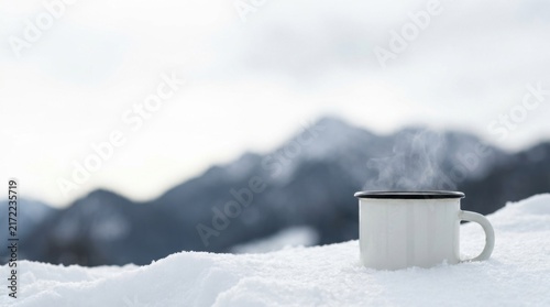 Enamel Camp Mug with Steaming Hot Drink in Snow with Mountain Range Background
