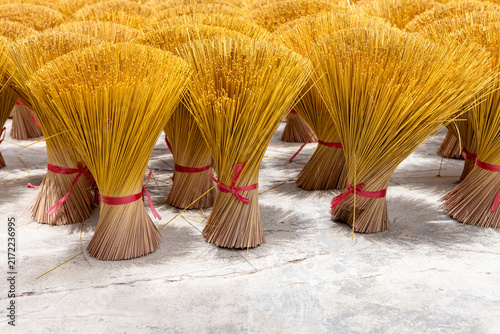 Bright yellow incense sticks bundled and tied with red ribbons stand upright on a concrete floor to dry, highlighting repetitive texture, handmade craft and traditional ritual objects with warm tones