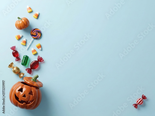Halloween candy spilling from pumpkin jar on blue background copy space