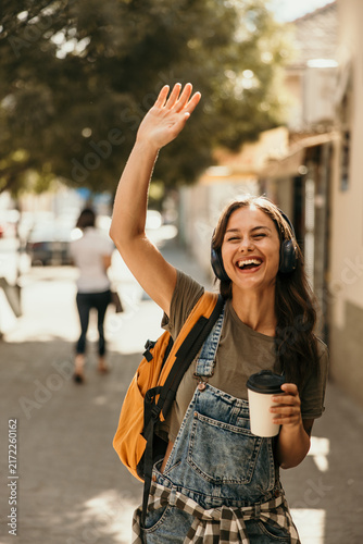 Young woman waving hello on a sunny street