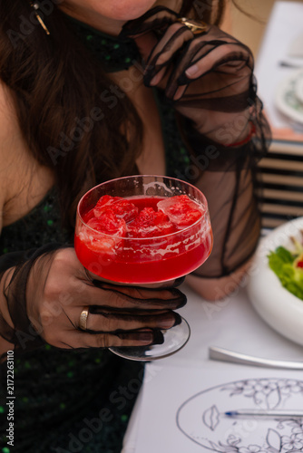Woman holds a cocktail with strawberries while sitting at a table with food