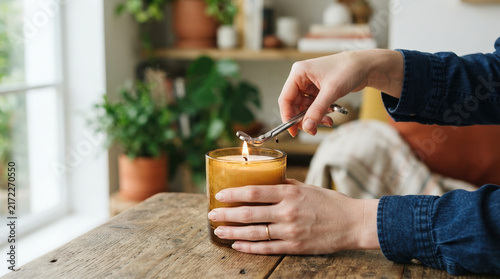 Hands trimming burning candle wick with metal trimmer. Person caring for scented soy candle in amber jar