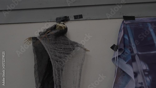 A hooded grim reaper with chains hangs by the house roof. A small skeleton ghost with gauze fabric is taped to the wall, creating a spooky Halloween yard decoration.