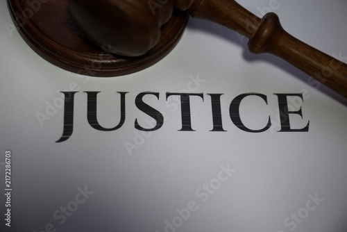 Wooden judge gavel resting above a paper with the word justice