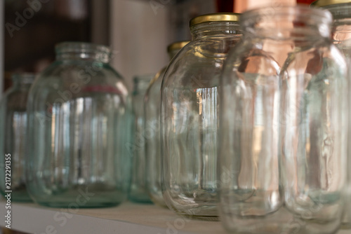 Empty clear glass jars of different sizes on a shelf prepared for home canning, food preservation, and pantry storage.