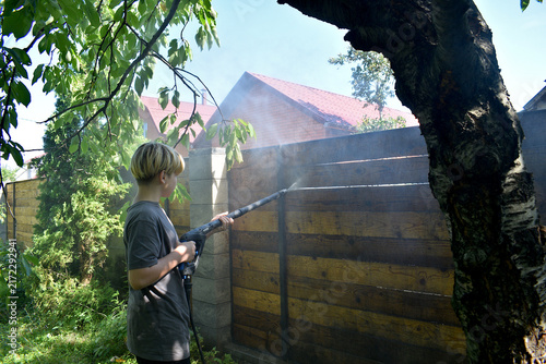 School-age boy washing wooden fence with pressure washer