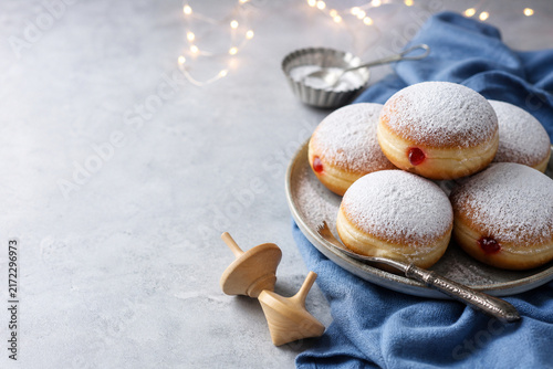 Hanukkah Sweetness: A delightful spread of sufganiyot, dusted with powdered sugar and filled with bright red jam, sits beside a wooden dreidel, evoking the festive spirit of Hanukkah celebrations.
