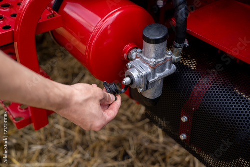 Hand removing protective rubber cap from a pneumatic valve and air tank on red agricultural machinery outdoors.