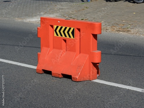 Bright orange road barricade positioned over white street lane marking for traffic control and safety.