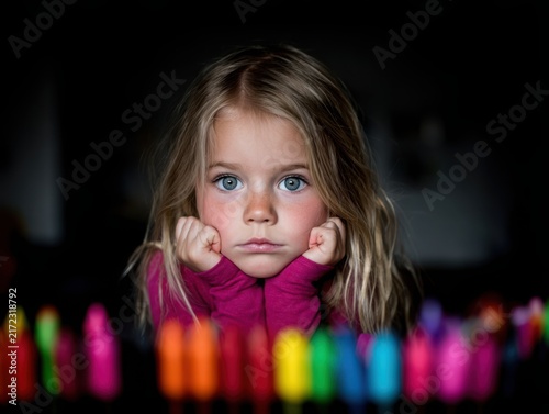 Young blonde girl resting her chin on her hands with colorful markers  