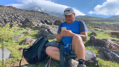 Tourist checking phone front view at a mountain rest stop on Mount Ararat, with backpack and rocky alpine terrain, showing trekking navigation, adventure travel, and outdoor recreation in Turkey