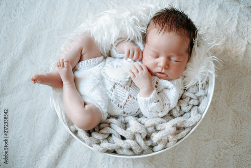 A newborn baby is sleeping in the crib; there's room for text. The little baby is sleeping sweetly.