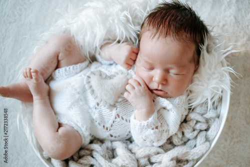 A newborn baby is sleeping in the crib; there's room for text. The little baby is sleeping sweetly.