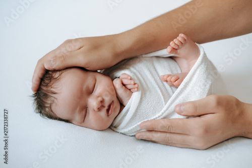 A newborn baby is sleeping in a diaper on a white, isolated background in the mother's arms; space for text. The mother gently embraces the small child with her arm.