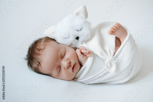 A newborn baby is sleeping sweetly in a diaper against a white, isolated background with a soft cat toy, space for text. Sweet sleep of a little child.