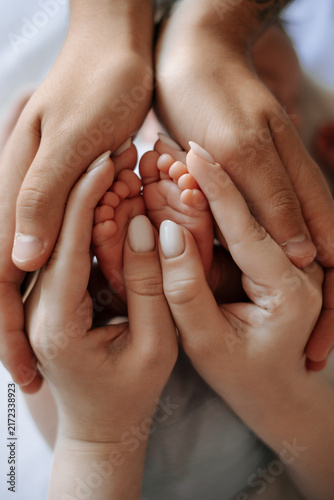 The legs of a small child, the legs of a newborn baby in their mother's arms, the mother's hands holding the baby's legs.