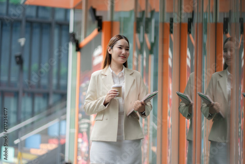 Happy workday concept. Smiling businesswoman walks with coffee and tablet in a modern office district. businesswoman, workday, coffee, professional, career, corporate lifestyle