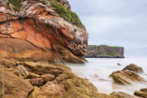 Rock formations and boulders along the shore of Playa de Andrín beach with white foam of crashing waves. Costa Verde, Asturias, Northern Spain.