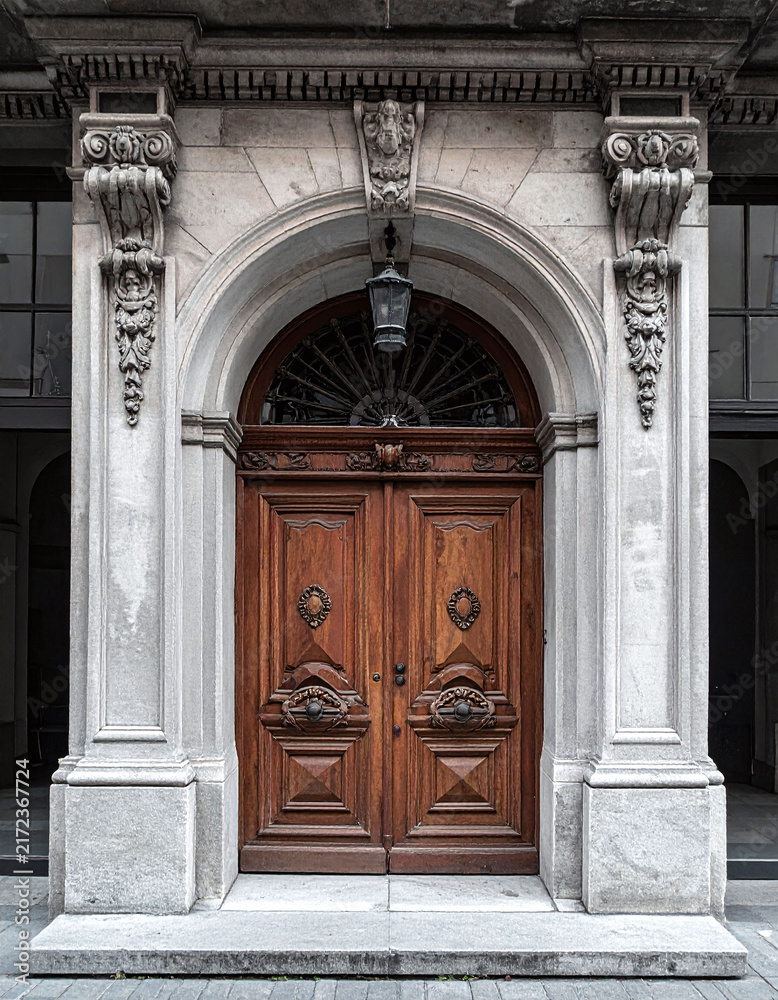 Obraz premium A grand, historic wooden door with intricate carvings stands framed by a majestic stone archway, evoking mystery and timeless elegance. Ideal for travel or architectural design. Nobody.