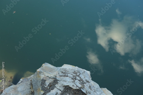 Dramatic steep cliff towering over a deep blue quarry lake on a bright sunny day