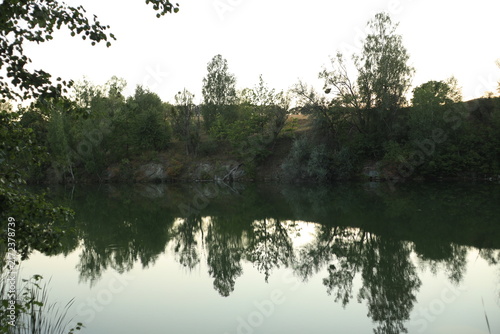Tranquil evening landscape of a flooded quarry lake surrounded by dense reeds and green trees at dusk