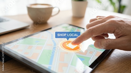 Person using a tablet to find local shops on a digital map with a shop local icon