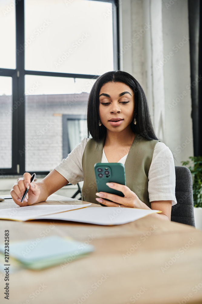 Obraz premium A woman concentrates on her phone while surrounded by papers and natural light.