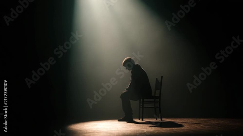 Empty dark space with an indistinct human silhouette seated on chair head bowed balanced lighting and shallow depth creating emotional weight and mental health symbolism