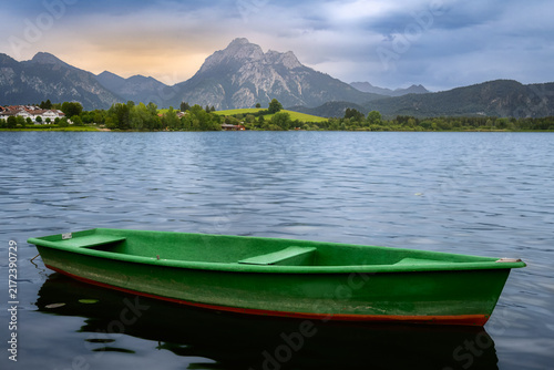 Green rowing boat on calm water of lake Hopfensee with mountain Saeuling at sunset
