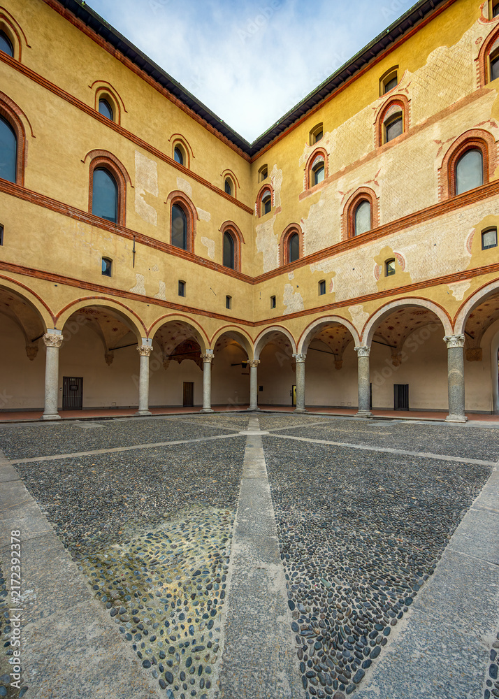 Fototapeta premium Milan, Italy, Castello Sforzesco courtyard with an arcade and a stone mosaic floor. Yellow walls with round-arched windows enclose the open area. 