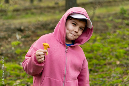 Enthusiastic smiling little child with chanterelle mushroom in his hand. Focus on the boy. Boy in pink hoodie showing edible mushroom he found in the forest. Weekend fun family activity.