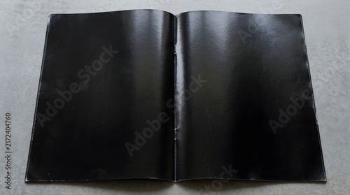 Open magazine with blank black pages laid flat on a grey concrete surface