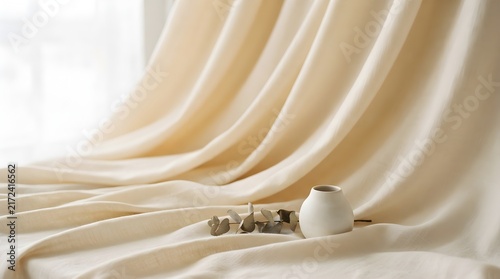 Minimalist white ceramic vase sitting gracefully upon soft beige fabric waves with a small dried eucalyptus sprig lying nearby peacefully