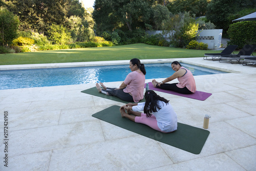 Diverse female family stretching on yoga mats beside pool on tiled patio with water bottle