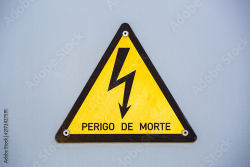 Perigo de Morte warning sign with a lightning bolt symbol, cautioning danger of death from electricity, mounted on a metal panel for safety awareness.
