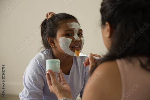 African American mother and teenage daughter applying mint mask from jar with flat brush at home