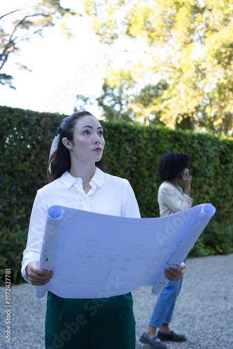 Obraz na płótnie Female colleagues holding rolled blueprints on site, foreground white blouse, on
