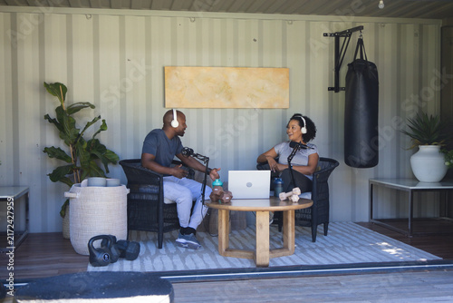 Diverse podcast co-hosts recording conversation in shipping container studio with laptop and mics