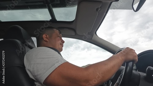 Man driving steering a car in side view during road travel, showing driver concentration, safe vehicle operation, personal mobility, transportation routine, and everyday automotive lifestyle