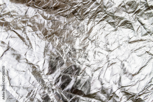 Silver crumpled aluminum foil texture with bright metallic reflections and sharp creases.
