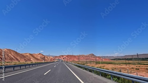 Highway drive through red mountains in wide road-level view, crossing arid Turkey landscape for travel, transport, road trip, logistics, destination marketing, and regional tourism promotion