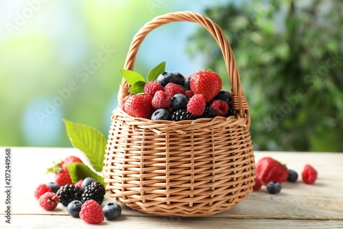 Canvastavla Many different berries in wicker basket on white wooden table, closeup