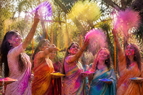 Group of Happy Indian Women in Traditional Sarees Celebrating Holi Festival Outdoors Throwing Colorful Powder Gulal into Air with Smiles and Joyful Energy