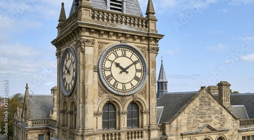 Historic stone courthouse clock tower with Roman numerals. Ornate municipal building architecture with intricate carvings against a blue sky