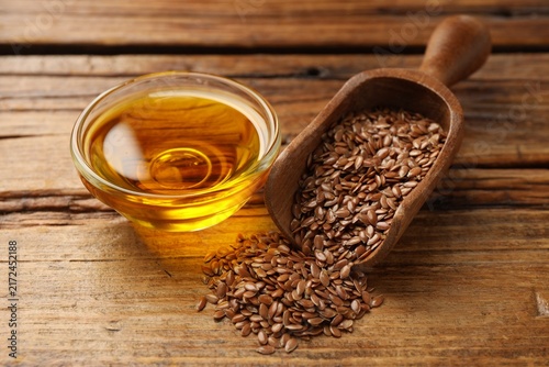 фотографія Flax seeds in scoop and bowl of oil on wooden table, closeup
