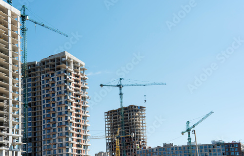 Modern apartment skyscrapers under construction with green cranes under clear sky
