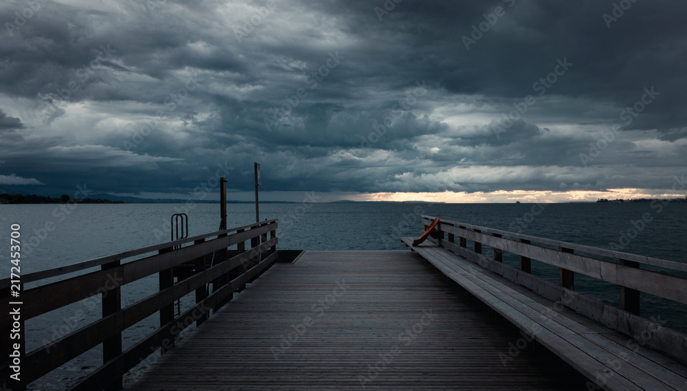 Fototapeta premium Wooden pier extends into calm waters under brooding sky