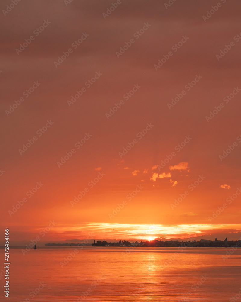 Fototapeta premium Orange sun dips low, painting sky and water in warm hues