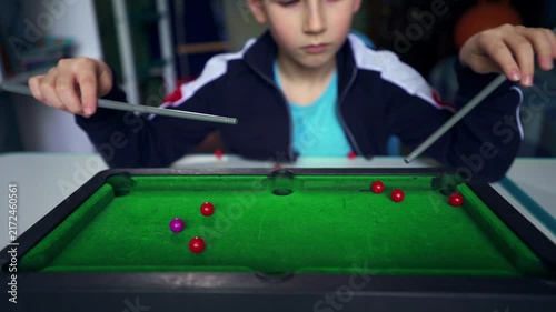 A seven-year-old boy spends his free time playing table billiards alone in his bedroom, illustrating childhood boredom, staying home, indoor leisure, quiet recreation, and ways to entertain himself