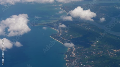 Aerial view over Phuket island tropical coastline with white clouds, green hills and turquoise Andaman Sea water on sunny day in Thailand. High angle wide shot.